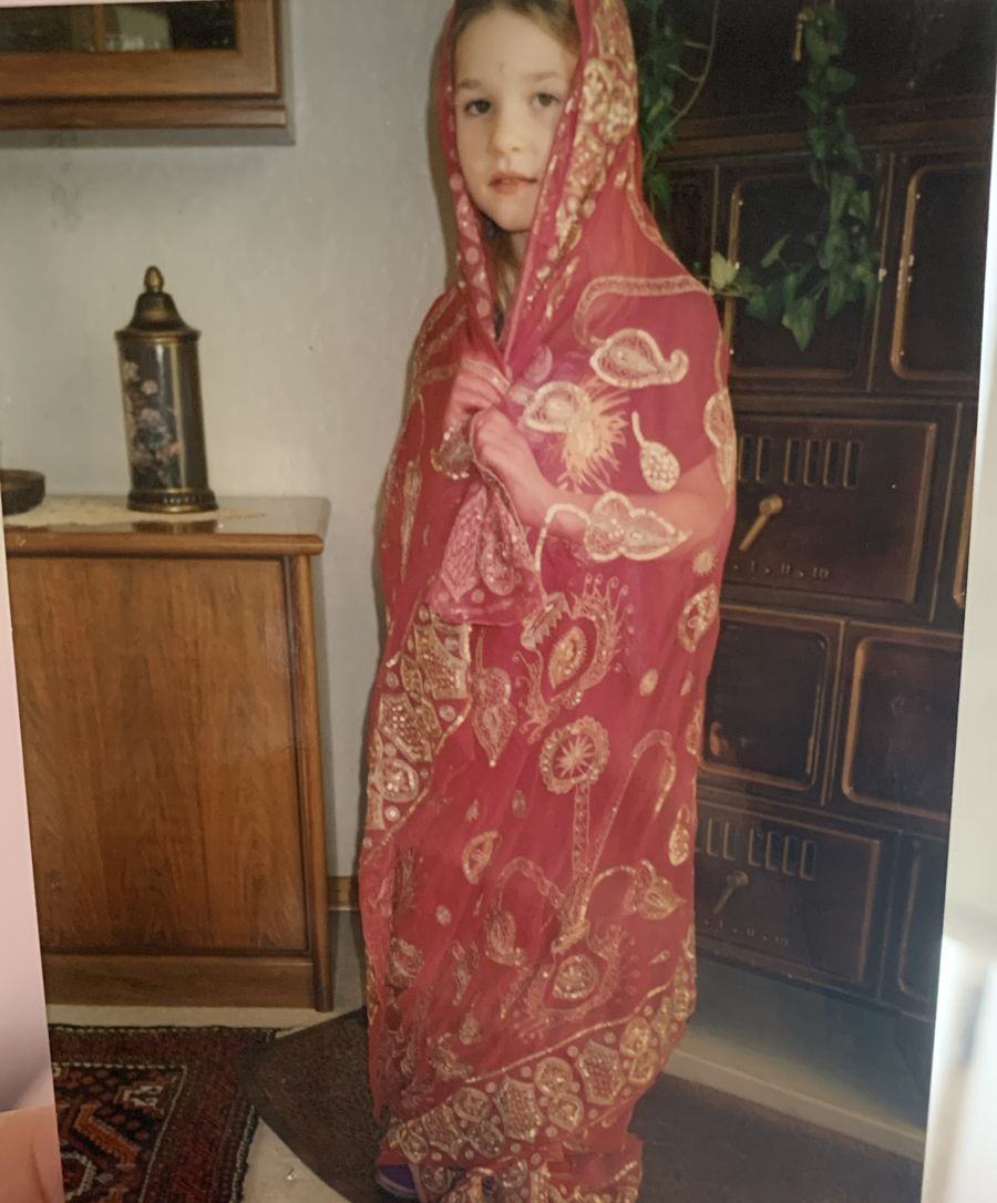 Alina als Kind, eingehüllt in ein rotes Tuch mit goldenen Pailletten