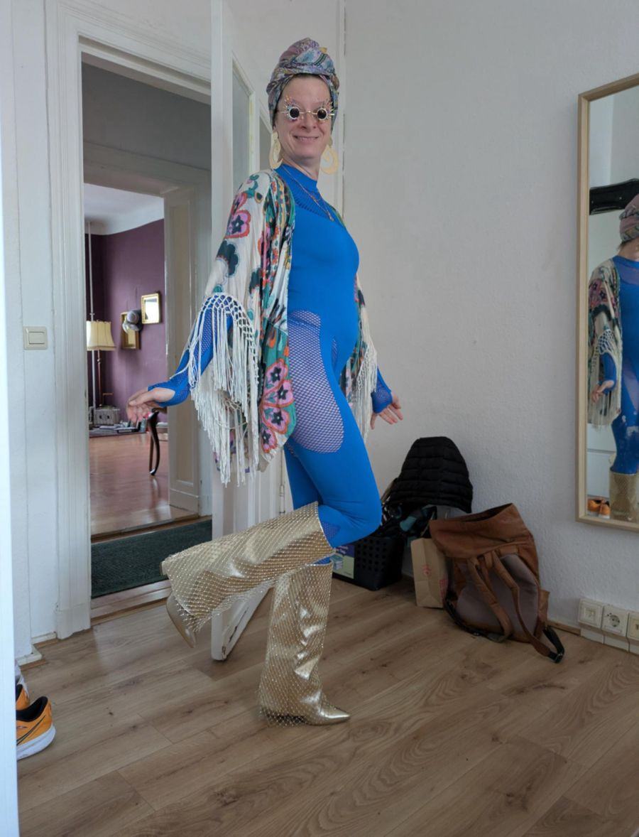 Marie vorher in blauem Catsuit, Fransen-Kimono, Turban und goldenen Stiefeln