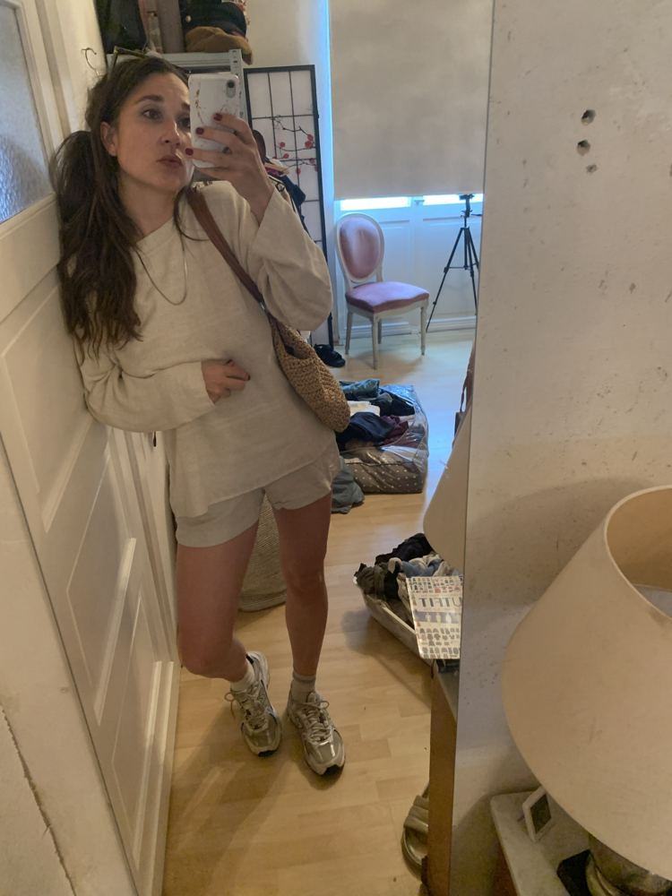 Alina im beigen Pullover und grauen Shorts vor dem Spiegel